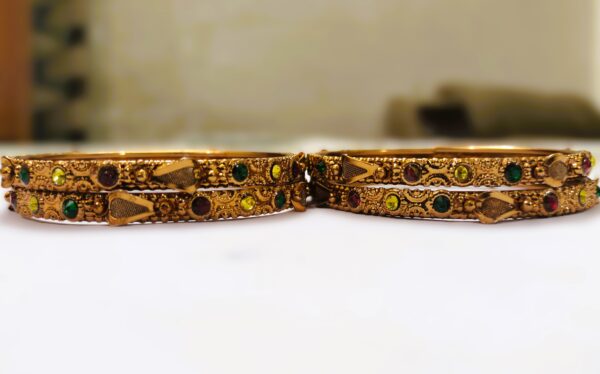 A close-up of the intricate designs and vibrant gemstones on the gold-plated bangles.