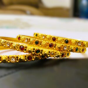 A close-up of the intricate designs and vibrant ruby, pink, and green gemstones on the gold-plated bangles.