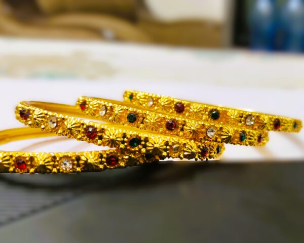 A close-up of the intricate designs and vibrant ruby, pink, and green gemstones on the gold-plated bangles.