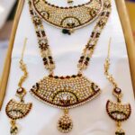 A stunning Rajasthani Royal Gold-Plated Bridal Jewelry Set, featuring a necklace, earrings, and a maang tika, adorned with vibrant gemstones and intricate designs.