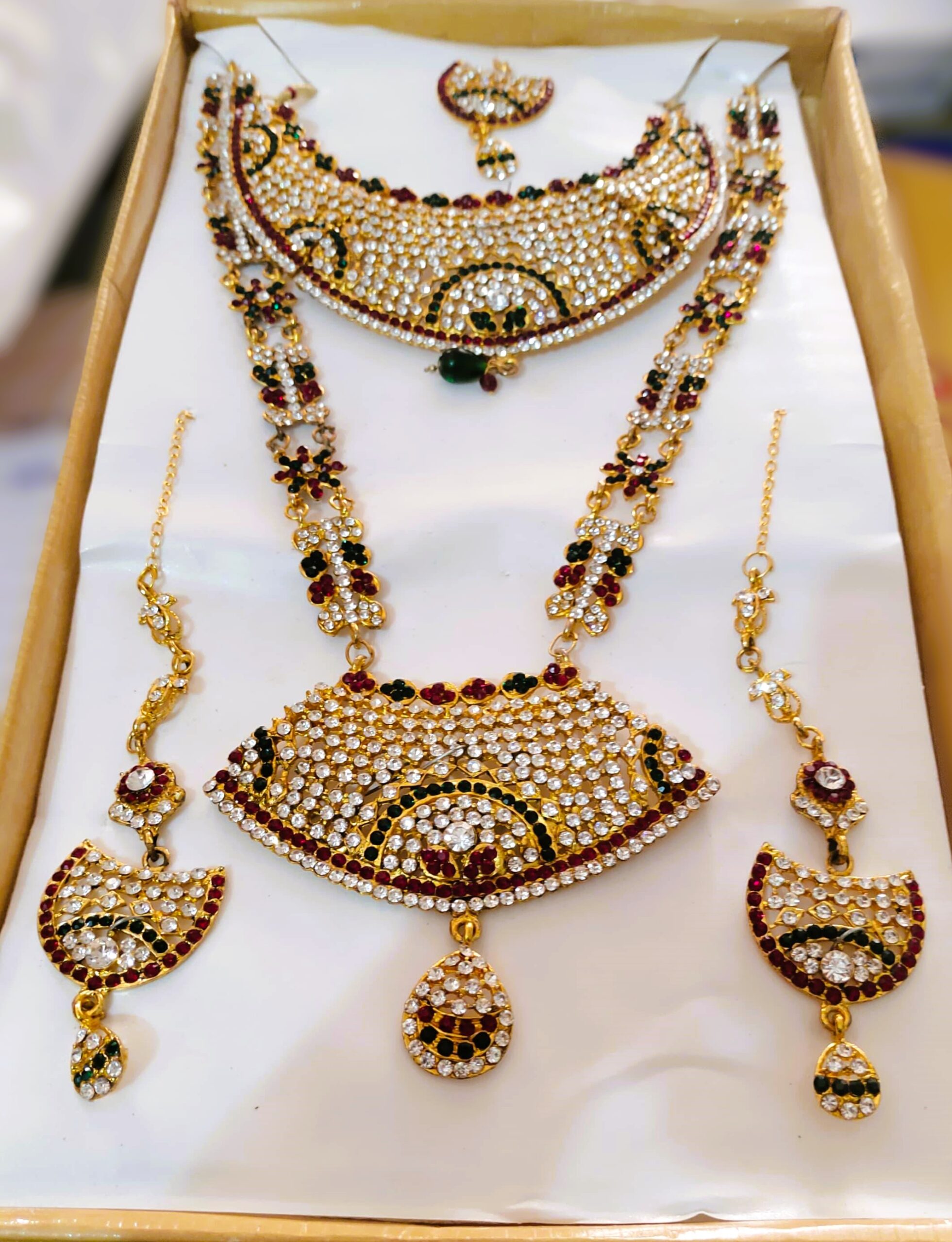 A stunning Rajasthani Royal Gold-Plated Bridal Jewelry Set, featuring a necklace, earrings, and a maang tika, adorned with vibrant gemstones and intricate designs.