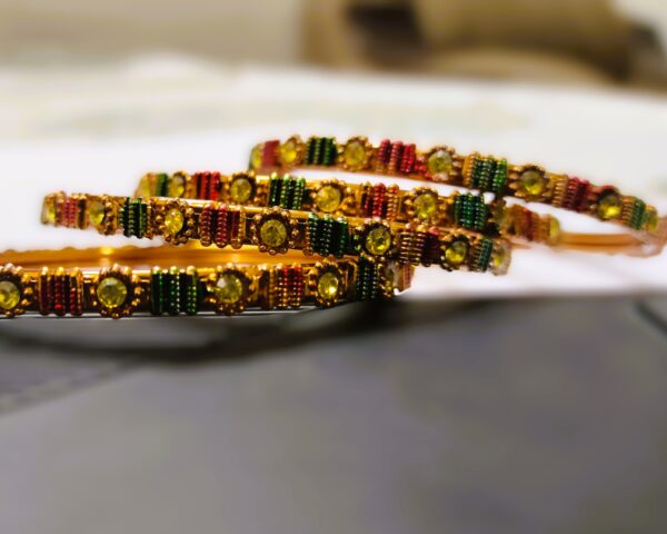 A close-up of the intricate designs and vibrant gemstones on the gold-plated bangles.