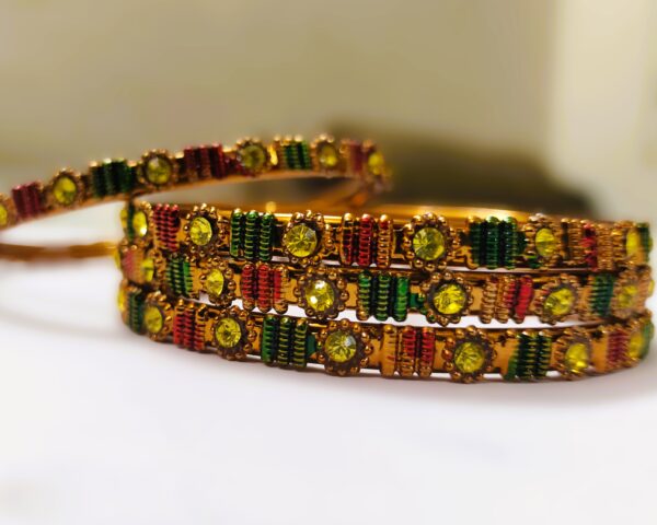 A close-up of the intricate designs and vibrant gemstones on the gold-plated bangles.