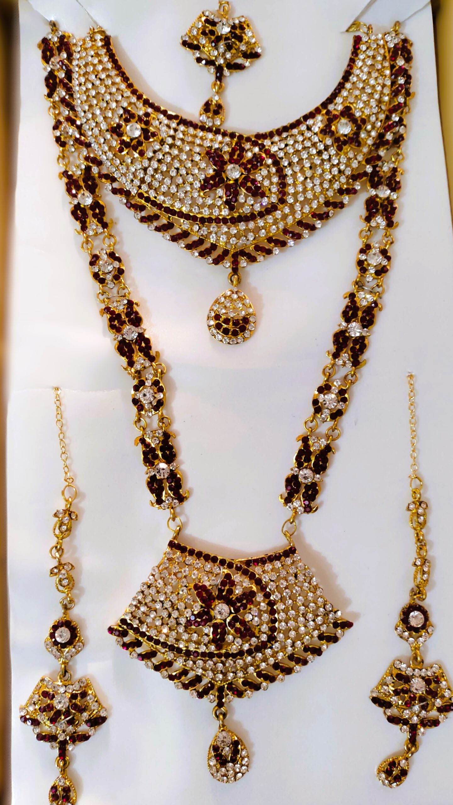 A stunning Rajasthani Royal Gold-Plated Bridal Jewelry Set, featuring a necklace, earrings, and a maang tika, adorned with crimson and ivory gemstones and intricate designs.