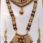 A traditional bridal jewelry set with necklace, earrings, maang tika, and choker, adorned with Kundan and American diamond stones.