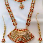 A stunning Rajasthani Royal Gold-Plated Bridal Jewelry Set, featuring a necklace, earrings, and a maang tika, adorned with red and white gemstones and intricate designs.