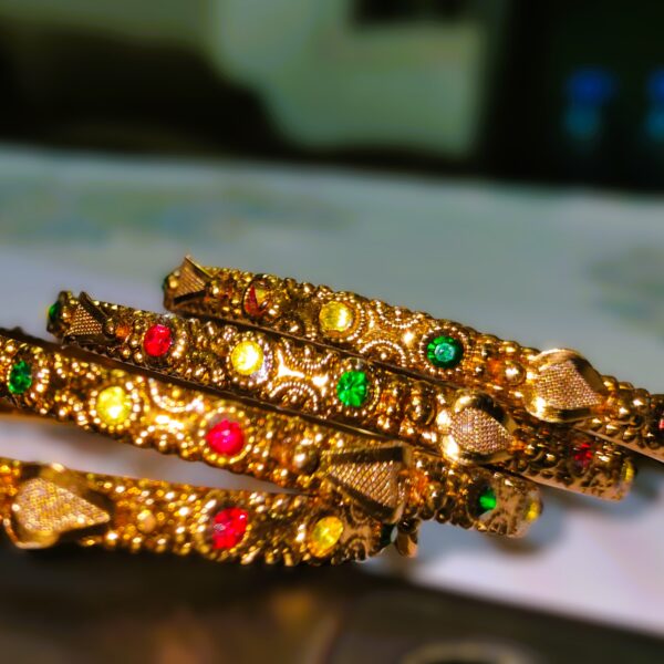 A close-up of the intricate designs and vibrant gemstones on the gold-plated bangles.