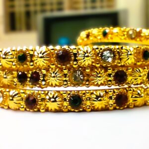 A close-up of the intricate designs and vibrant ruby, pink, and green gemstones on the gold-plated bangles.