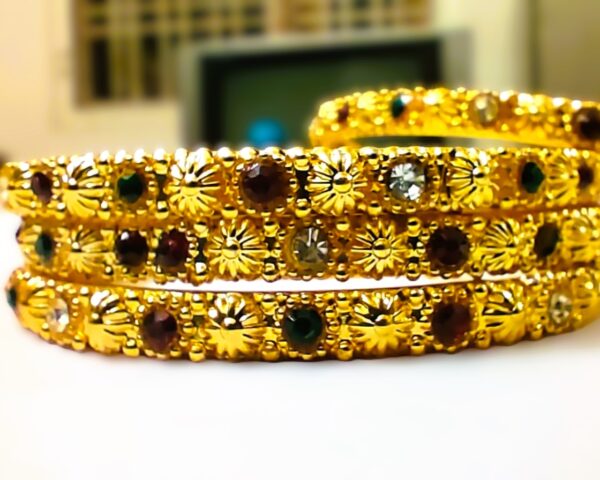 A close-up of the intricate designs and vibrant ruby, pink, and green gemstones on the gold-plated bangles.