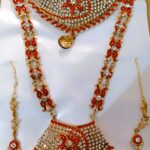 A stunning Rajasthani Royal Crimson and Ivory Bridal Jewelry Set, featuring a necklace, earrings, and a maang tika, adorned with intricate designs and vibrant gemstones.