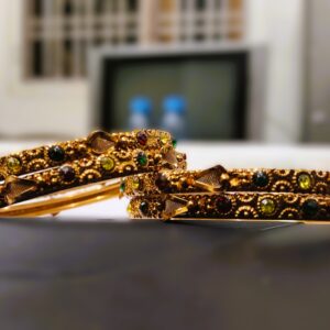 A close-up of the intricate designs and vibrant gemstones on the gold-plated bangles.