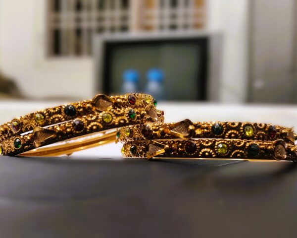 A close-up of the intricate designs and vibrant gemstones on the gold-plated bangles.