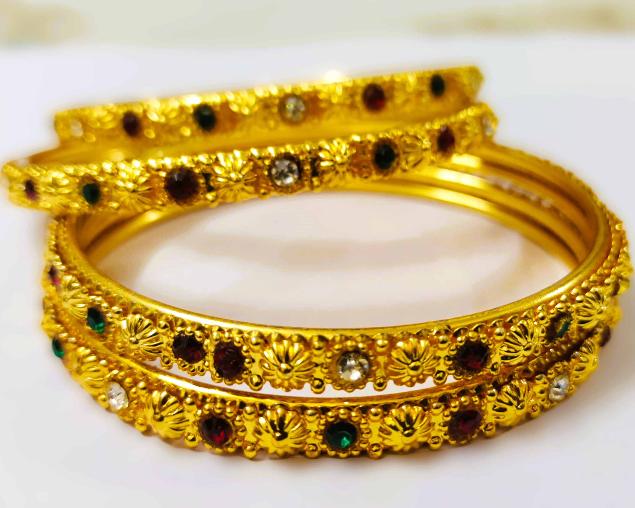 An Anaka Traditional Gold-Plated Bangle Set with intricate designs and vibrant ruby, pink, and green gemstones, perfect for any occasion.