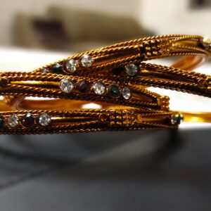 A close-up of the intricate designs and vibrant gemstones on the copper bangles.