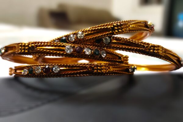 A close-up of the intricate designs and vibrant gemstones on the copper bangles.